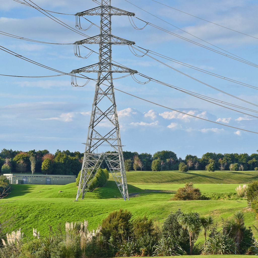 A vertical shot of high voltage electric tower with green meadow in the foreground